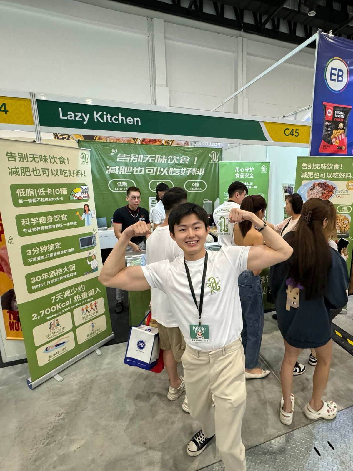 Jun flexing at the Lazy Kitchen booth, with visitors trying Lazy Diet meals behind him